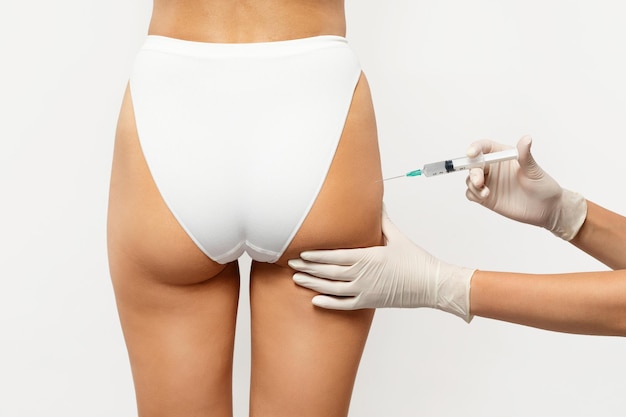 Primer plano de un profesional de la salud con guantes administrando una inyección en la parte superior del muslo