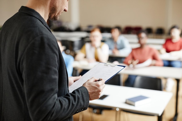 Primer plano de un profesor universitario masculino revisando notas mientras da una conferencia a los estudiantes en la copia del aula