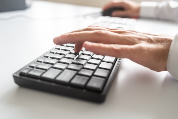 Foto primer plano de un programador de negocios utilizando el teclado y el ratón de la computadora para trabajar en un proyecto.