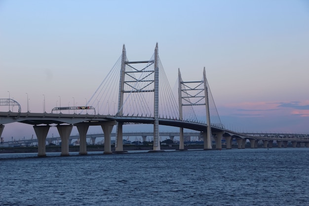 Primer plano del puente del cable y la autopista sobre la bahía contra el cielo de la tarde con reflejos rojos del sol poniente sin detenerse en la señal de la autopista