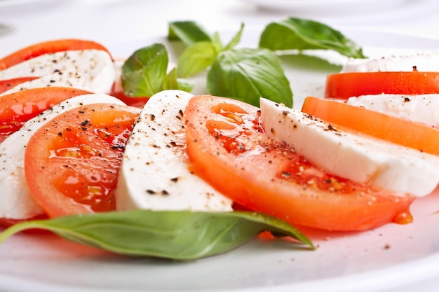 Primer plano de queso y tomates con hojas de albahaca en un plato