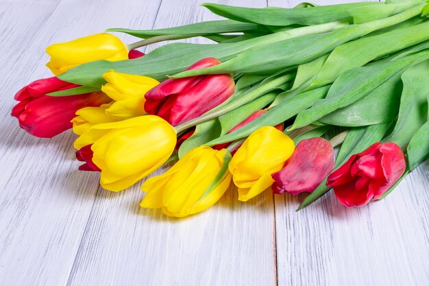 Primer plano de un ramo de tulipanes de primavera amarillos y rojos se encuentra sobre una mesa con una superficie de madera clara.