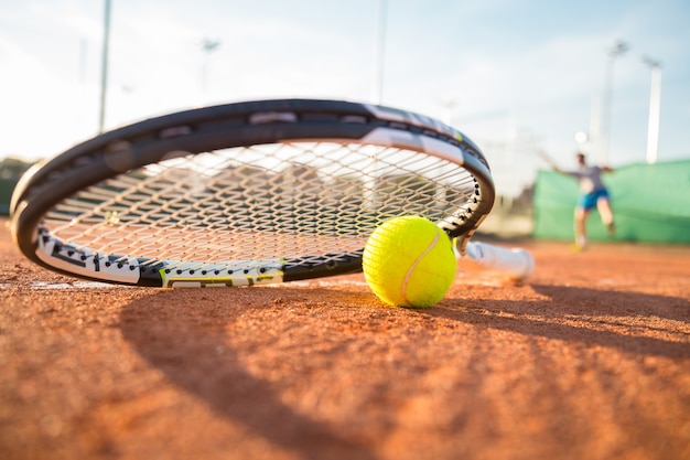 Foto primer plano de la raqueta de tenis y la pelota colocada en la cancha mientras el jugador golpea la pelota.