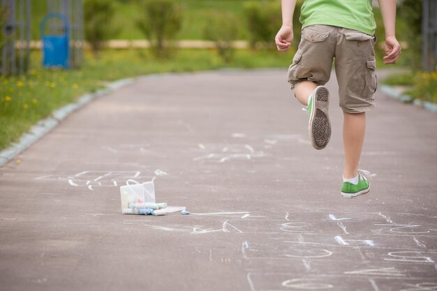 Primer plano de rayuela dibujada con tiza en la carretera asfaltada y niño saltando Juegos infantiles