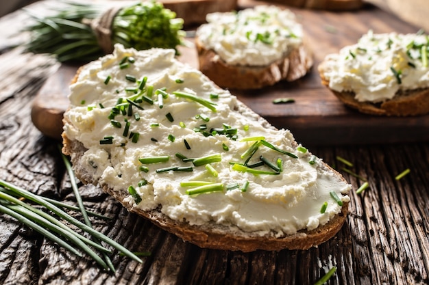 Primer plano de la rebanada de pan con la tradicional bryndza eslovaca para untar hecha de queso de oveja con cebollino recién cortado colocado sobre madera rústica.