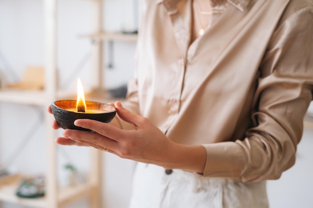 Primer plano recortado de una joven irreconocible sosteniendo una vela hecha a mano en las manos. Primer plano de una mujer sosteniendo velas relajantes aromáticas en casa. Concepto de bienestar y relajación.