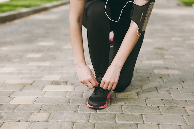 Primer plano recortado de las manos de la mujer atando los cordones de los zapatos en zapatillas negras y rosadas para trotar o entrenar en el camino al aire libre