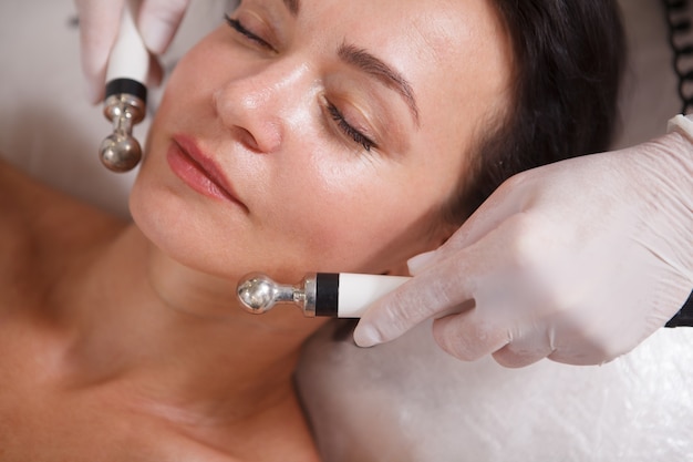 Primer plano recortado de una mujer madura disfrutando de un facial de microcorriente en un salón de belleza