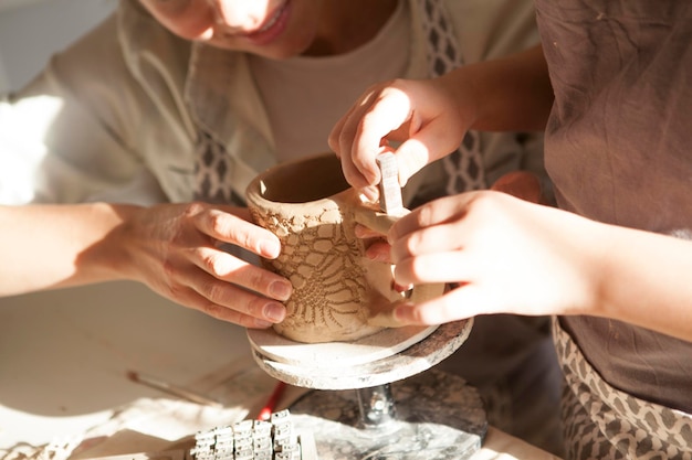 Primer plano recortado de un niño y una madre decorando una taza de cerámica con sellos