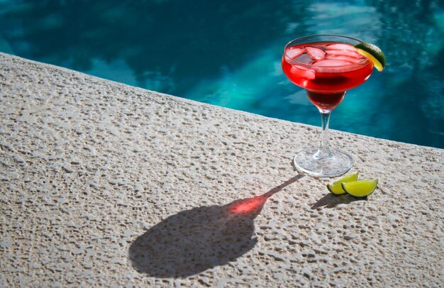 primer plano de un refrescante cóctel rojo con limas verdes en la piscina