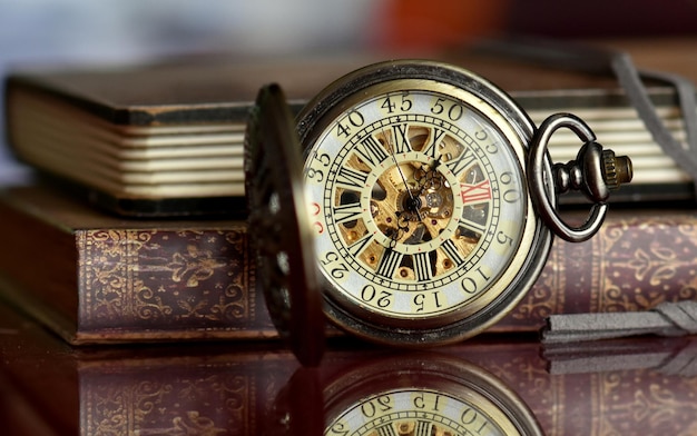 Primer plano de un reloj de bolsillo con libros en la mesa