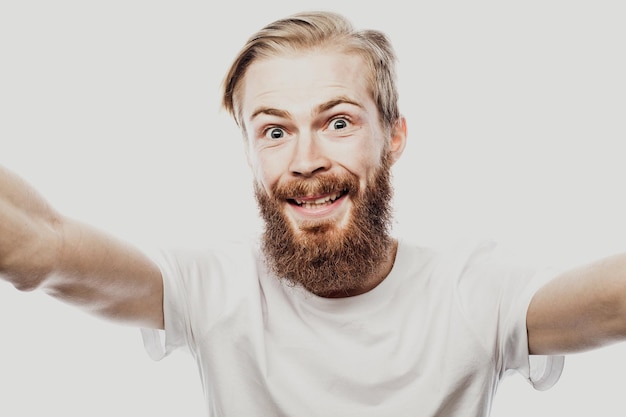 Primer plano retrato de un alegre hombre barbudo tomando selfie sobre fondo blanco.