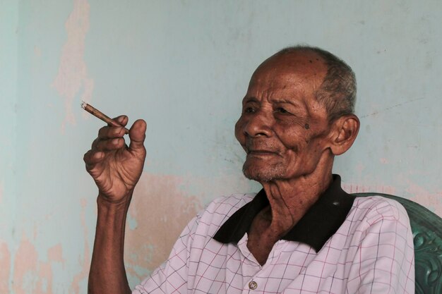 Primer plano retrato de un anciano javanés asiático con un cigarrillo en la mano