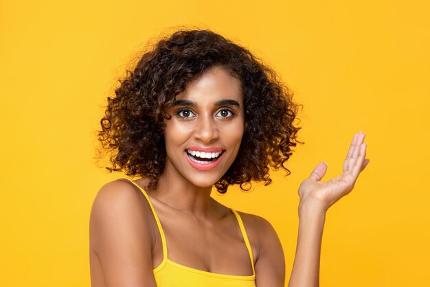 Foto primer plano retrato de una atractiva mujer afroamericana sonriente con una mano levantada mirando a la cámara aislado estudio fondo amarillo