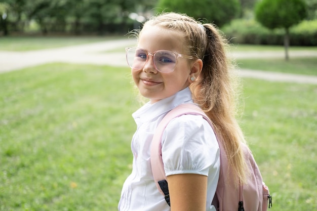 primer plano retrato de colegiala rubia en gafas camisa blanca con mochila rosa regreso a la escuela