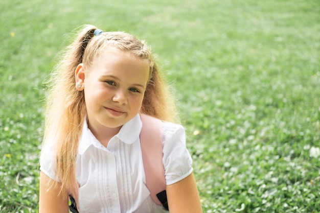 primer plano retrato de una colegiala rubia sonriente con camisa blanca con mochila rosa de regreso a la escuela