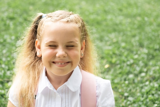 primer plano retrato de una colegiala rubia sonriente con camisa blanca con mochila rosa de regreso a la escuela