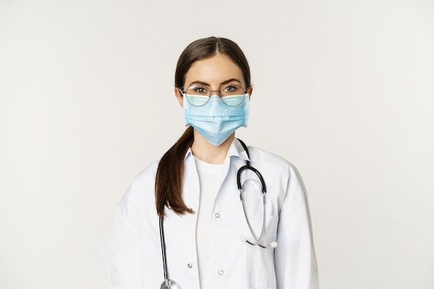 Primer plano retrato de una doctora del personal del hospital con gafas y mascarilla médica que parece seria...