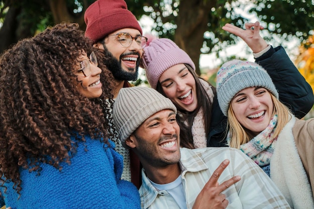 Primer plano retrato de un grupo de jóvenes caras sonriendo y divirtiéndose juntos Amigos felices multirraciales con sombreros abrigos y ropa otoñal disfrutando de un día de fin de semana Concepto de estilo de vida