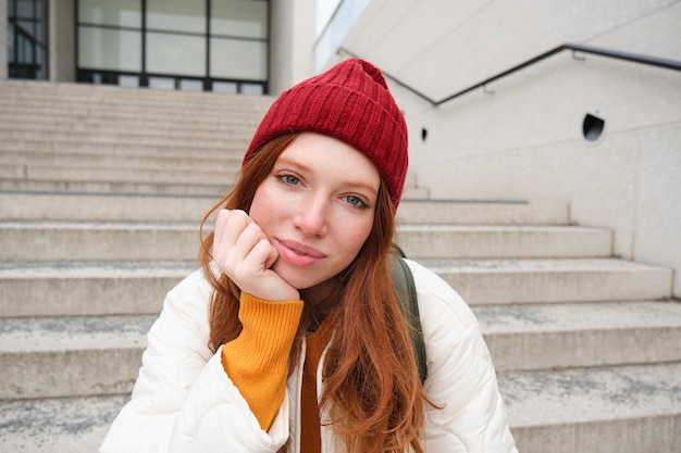 Primer plano retrato de hermosa chica pelirroja con sombrero rojo mujer urbana con pecas y pelo de jengibre sentarse