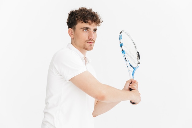 Primer plano retrato de hombre confiado en camiseta mirando a un lado y sosteniendo la raqueta mientras juega al tenis aislado sobre la pared blanca