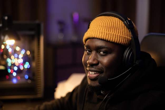 Primer plano retrato de hombre sonriente de piel oscura con gorra amarilla con auriculares cuarto oscuro por la noche