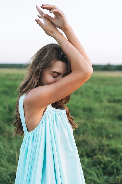 Primer plano retrato de joven hermosa mujer de cabello largo despreocupada en vestido azul turquesa claro en el campo del atardecer Sensibilidad al concepto de naturaleza feminidad