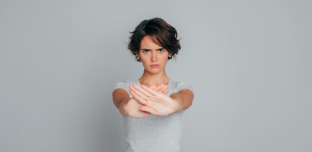 Foto primer plano retrato de una joven mujer seria y segura con ropa informal muestra palmas cruzadas sin parar símbolo prohibido o signo aislado sobre fondo gris