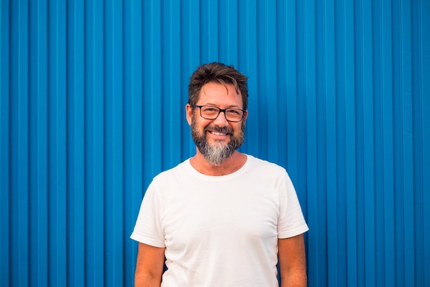 Primer plano y retrato de joven sonriendo y mirando a la cámara - pared azul en el fondo - concepto y estilo de vida de gente feliz