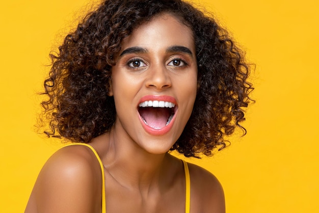 Primer plano retrato de mujer afroamericana feliz mirando a la cámara con la boca abierta en un estudio aislado de fondo amarillo