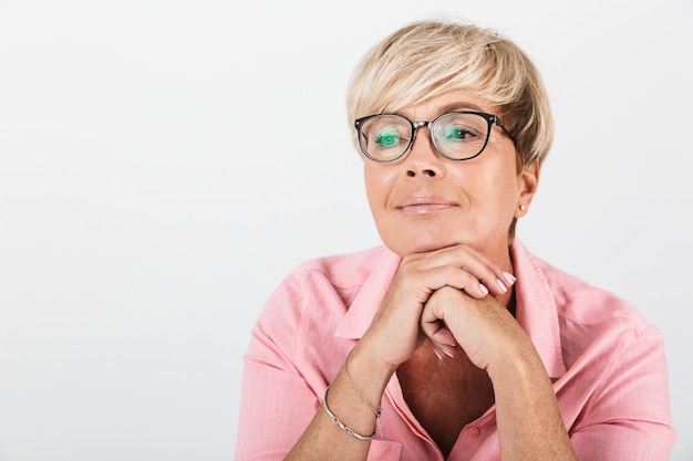 Primer plano retrato de mujer caucásica de mediana edad con el pelo rubio corto con anteojos mirando a la cámara aislada sobre la pared blanca