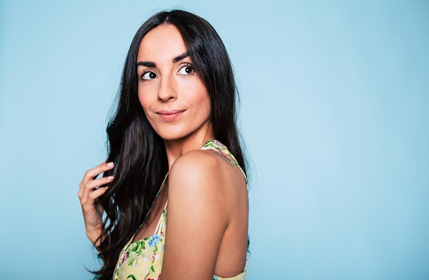 Foto primer plano retrato de mujer morena encantadora en vestido sobre fondo azul.