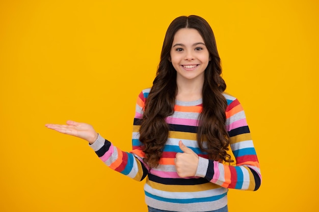 Primer plano retrato de niña adolescente mostrando en el espacio de la copia apuntando a anuncios publicitarios aislados sobre fondo amarillo Adolescente feliz emociones positivas y sonrientes de niña adolescente