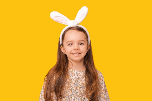 Primer plano retrato de una niña encantadora sonriendo a la cámara lista para la fiesta de Pascua Foto de estudio sobre fondo amarillo