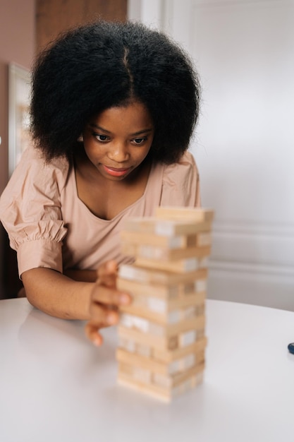 Primer plano retrato vertical de una mujer afroamericana seria jugando torre con diversos amigos sacando una cuadra de la torre tambaleante