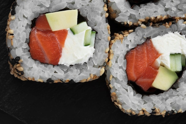 Primer plano de rollos de sushi uramaki con caviar rojo, salmón, atún y aguacate sobre un fondo negro