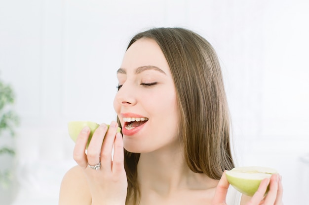 Primer plano rostro de mujer hermosa con piel limpia fresca y saludable, comer una manzana, posando y sonriendo. Aislado sobre fondo blanco