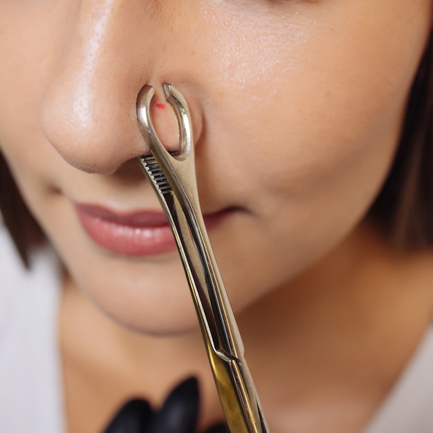 Primer plano del rostro de una mujer joven con piercing colgando de su nariz.