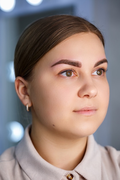 Un primer plano del rostro de una mujer joven que acaba de hacerse un tatuaje permanente en una ceja.
