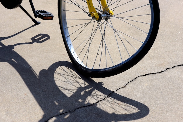 Primer plano de una rueda de bicicleta torcida, proyectando sombras surrealistas en la acera