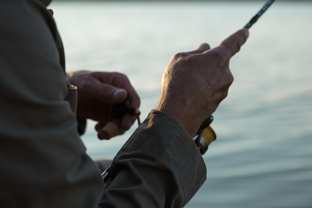 Foto primer plano de la rueda de la caña de pescar, hombre pescando con una hermosa puesta de sol.