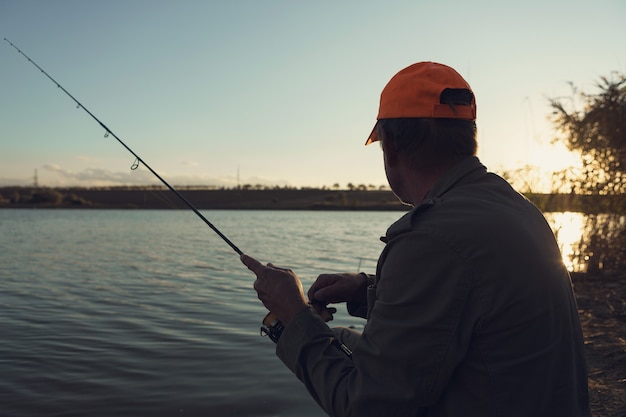 Primer plano de rueda de caña de pescar, hombre pescando con una hermosa puesta de sol.