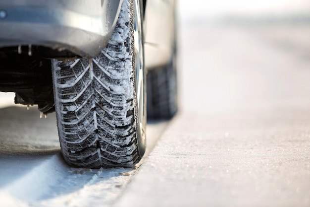 Primer plano de la rueda del coche en neumático de invierno en carretera nevada