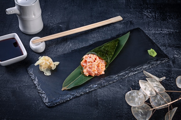 Primer plano de sabroso sushi roll de mano con salmón y caviar Tobico servido en plato de piedra oscura con salsa de soja y jengibre. Copia espacio Temaki, cocina japonesa. Comida sana