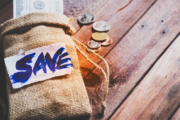 Primer plano de un saco con texto guardado y monedas en una mesa de madera