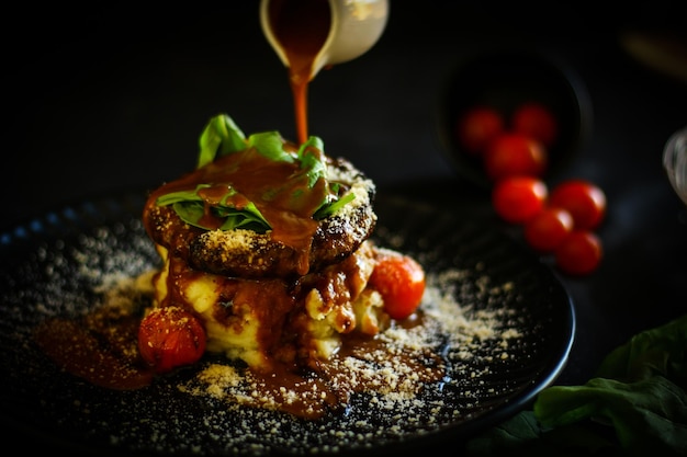 Primer plano de la salsa que se vierte sobre la comida servida en un plato contra un fondo negro