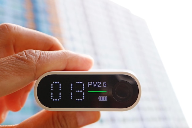 Primer plano de un sensor de calidad del aire en la mano con un grupo de edificios altos en el fondo