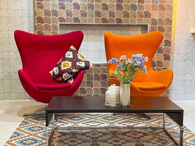 Primer plano de una silla moderna roja y naranja con un jarrón de flores en una mesa negra en una casa moderna