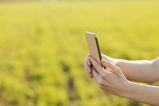 Primer plano de smartphone en manos de una niña contra la pared de un campo verde.