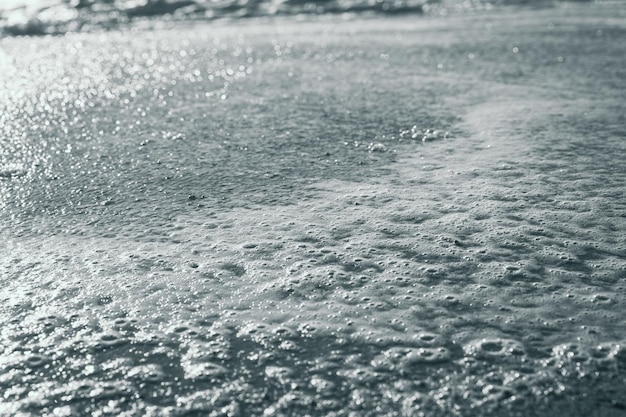 Primer plano sobre la espuma en la costa del mar con el reflejo del sol sobre el agua Concepto de fondo abstracto